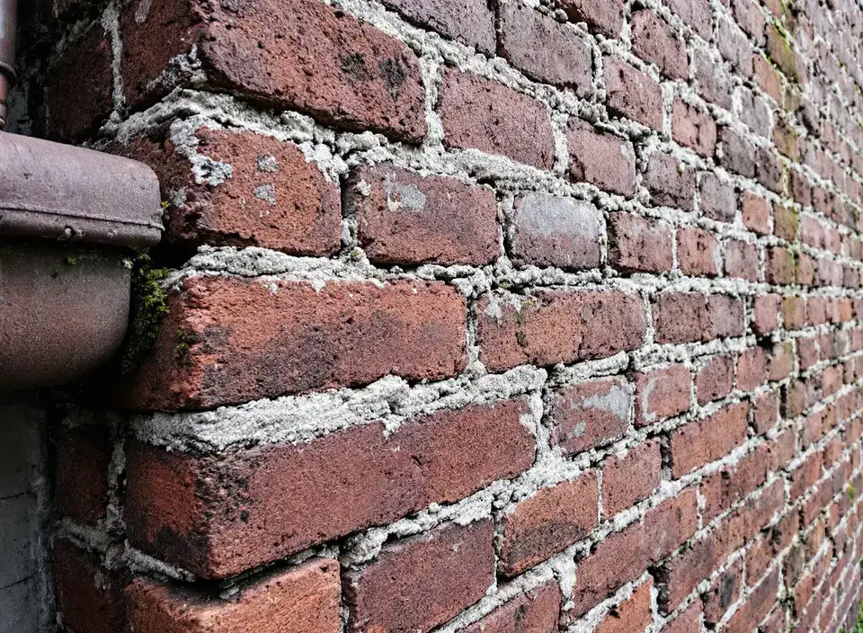 Oude bakstenen muur van dichtbij, met verweerde en deels gescheurde voegen en wat mos bij de regenpijp